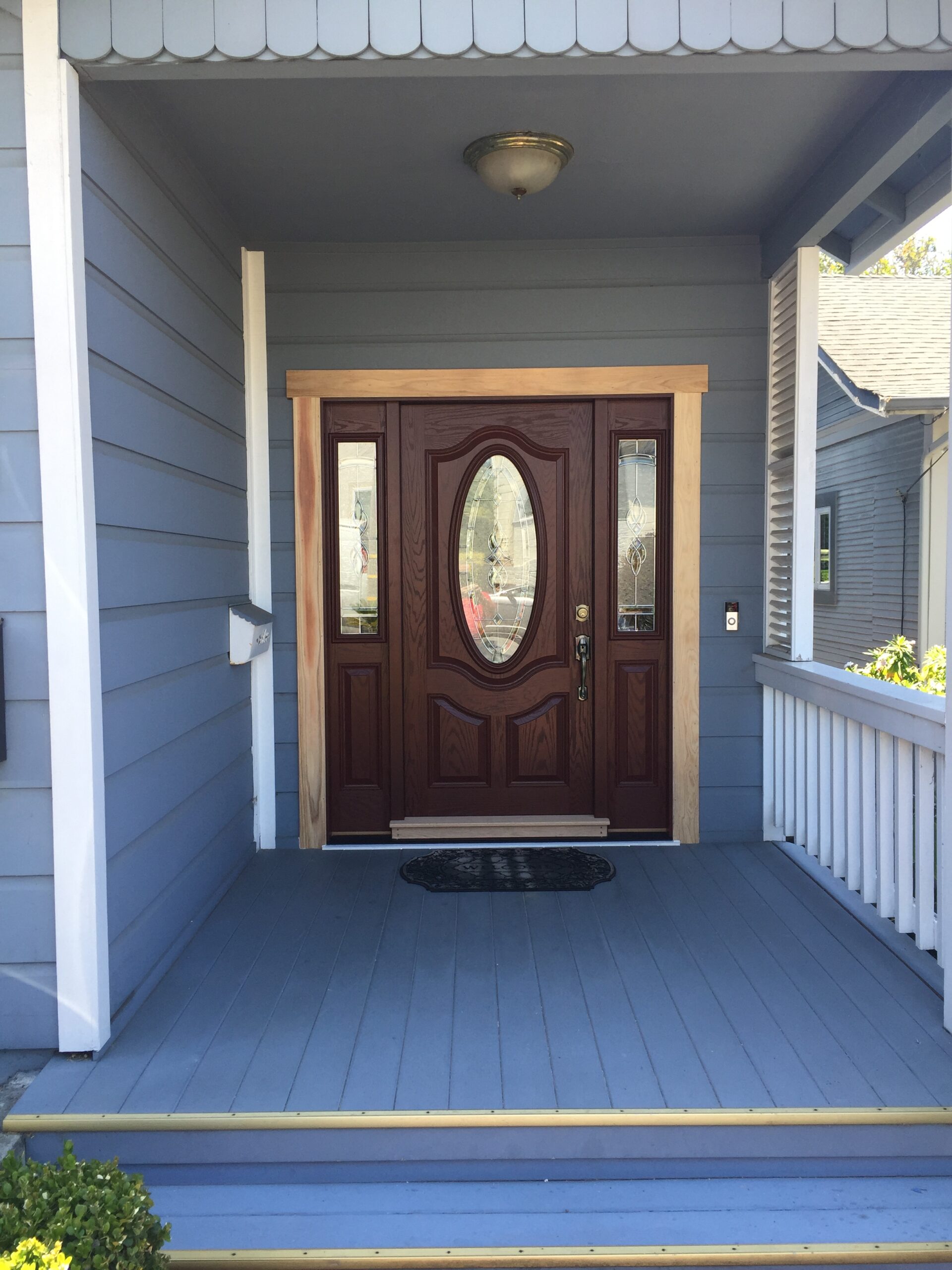 Detailed brown front door with glass panels on a light blue house
