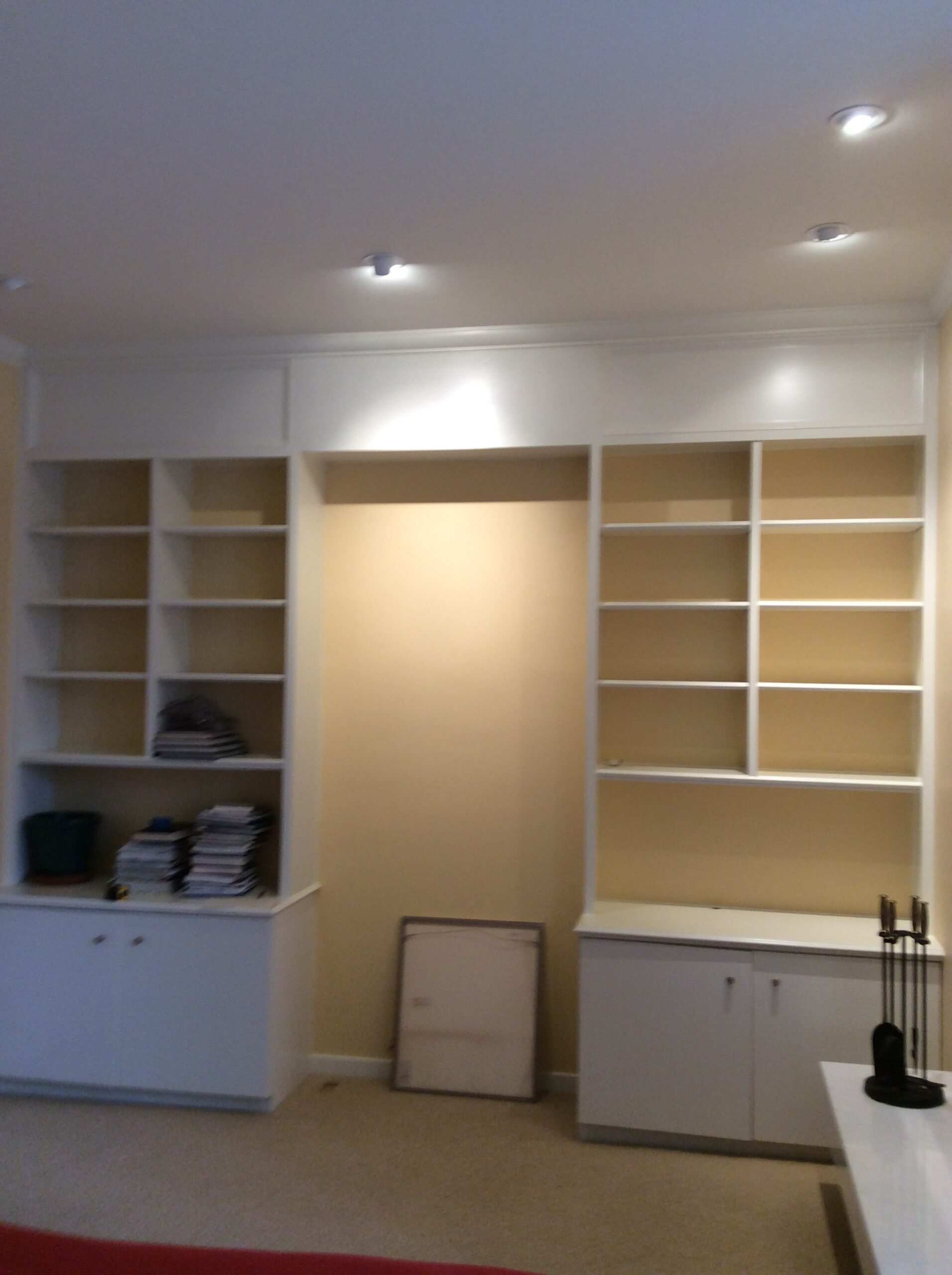 Neutral-colored room featuring built-in white shelves. One side is filled with books and decorative items; the center space is empty, awaiting organization.